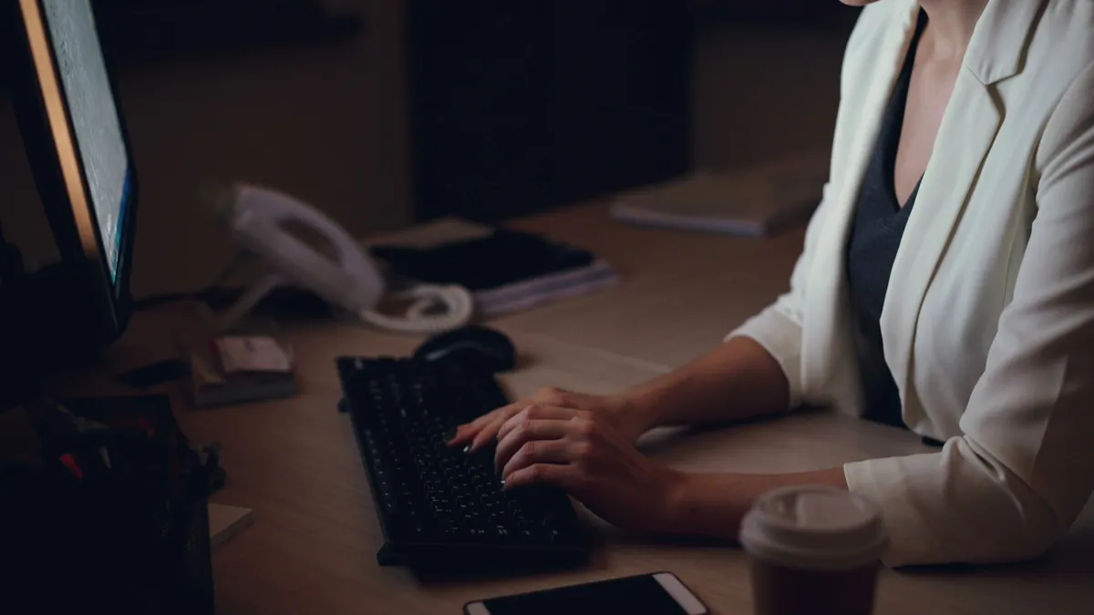 Hands at a keyboard on a desk late at night, a coffee cup beside them.