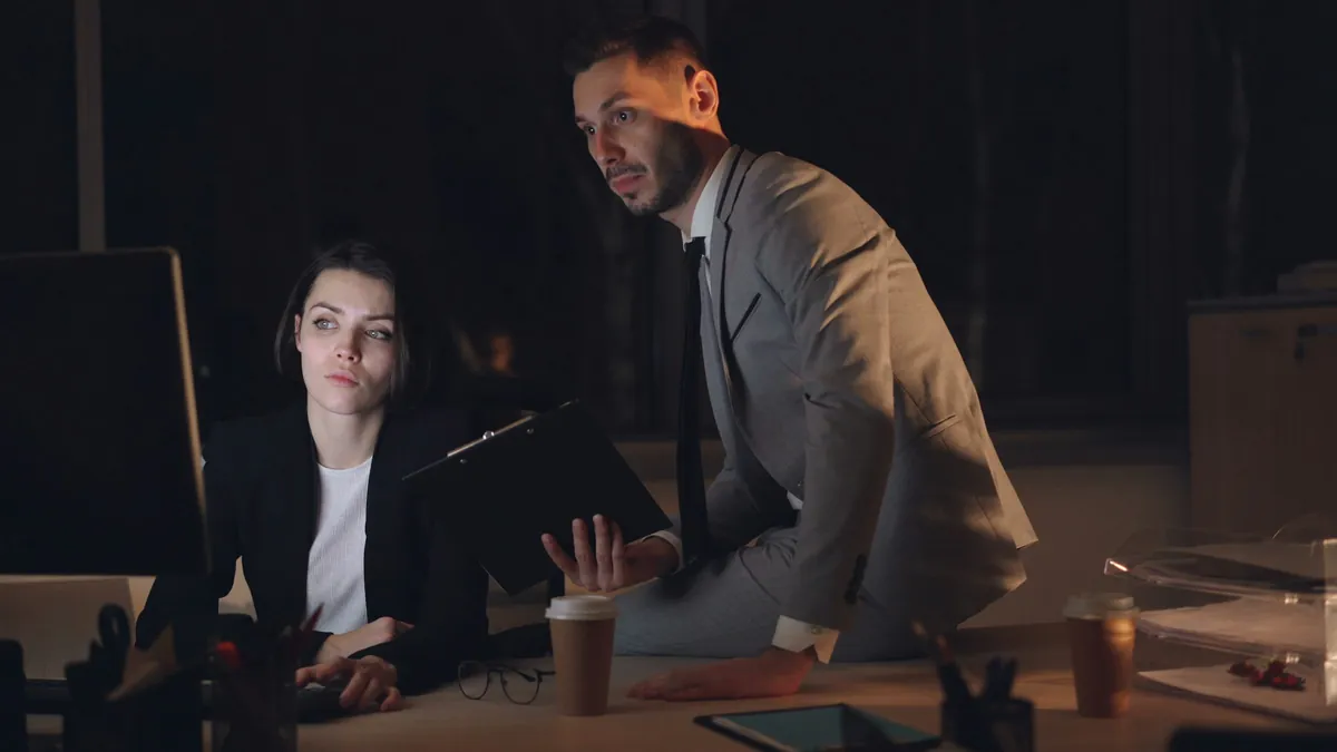 Late at night, a colleague leans over an associate’s desk to go through the work.